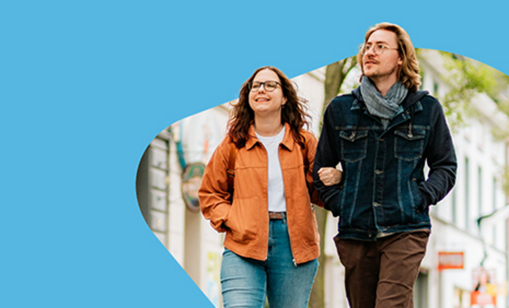 Zu sehen sind zwei Menschen, welche durch eine Stadt laufen.